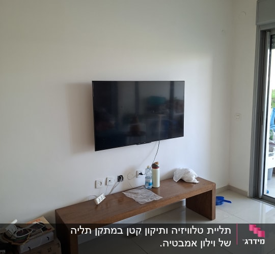 טלוויזיה מותקנת על קיר עם שולחן עץ וכבלים